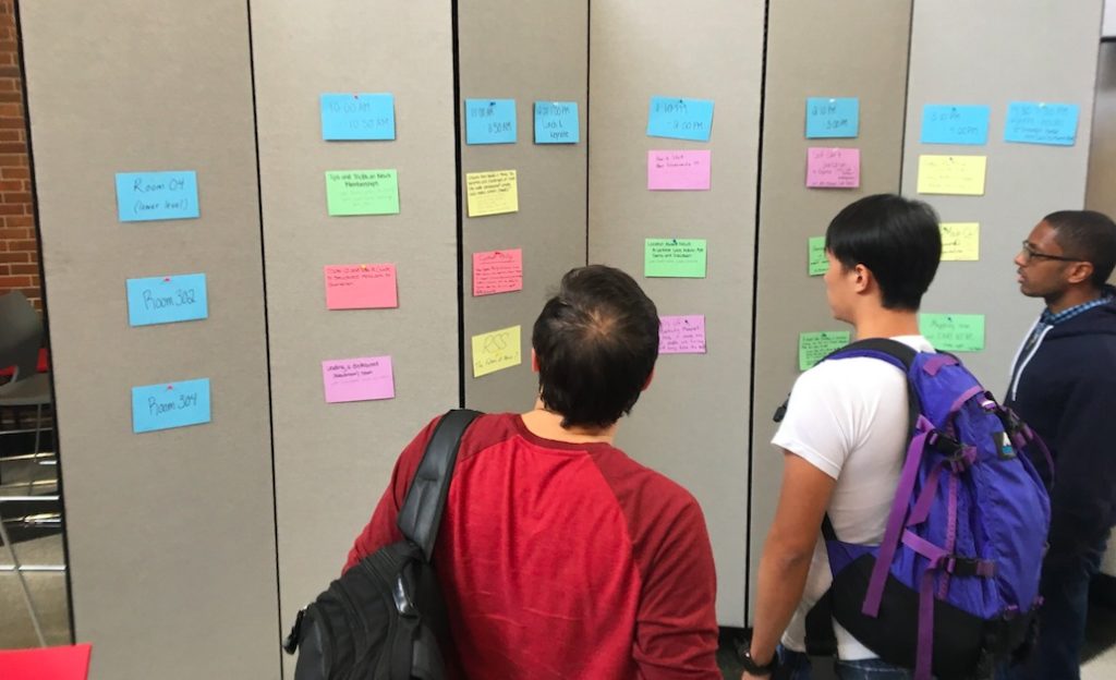Bright index cards on a tack board with people standing in front of it